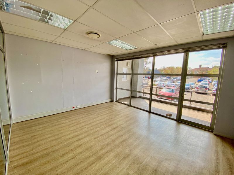 A vacant commercial office space featuring laminate flooring, a suspended ceiling with recessed lighting, and large windows providing ample natural light.