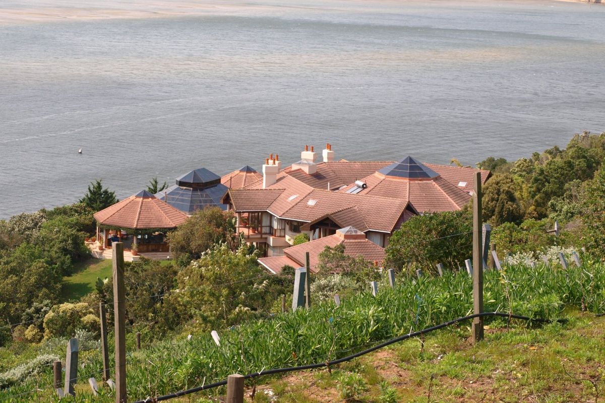 An elevated aerial view of a large residential property with a tiled roof, chimneys, and a gazebo, situated overlooking a coastal landscape.