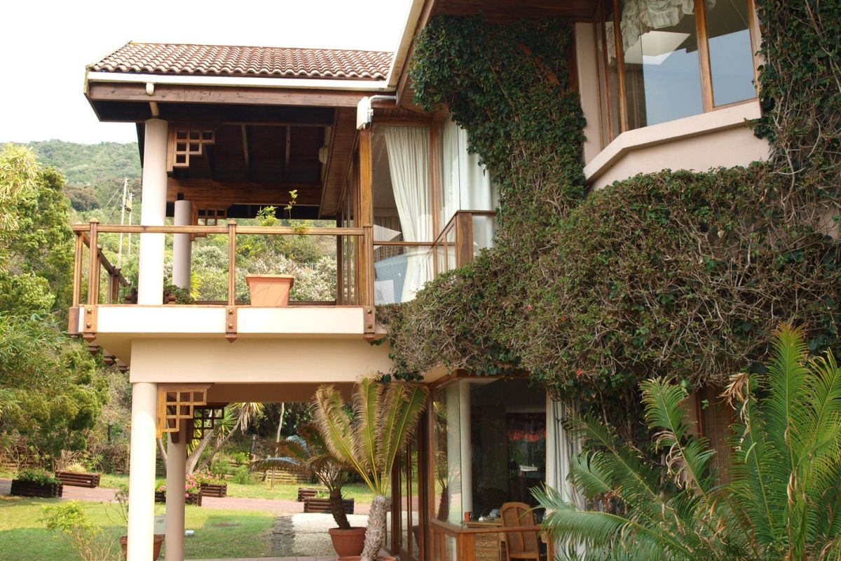 Rear elevation of a multi-level farm property featuring a covered balcony, timber detailing, and extensive garden views with established climbing greenery.