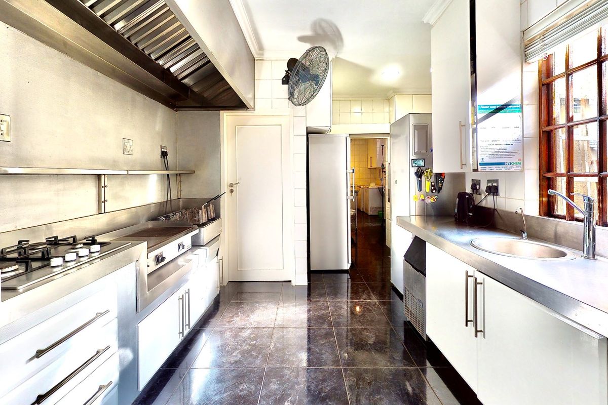A functional commercial-style kitchen featuring stainless steel countertops, a gas cooktop, an extractor hood, and ample built-in cabinetry with tiled finishes.