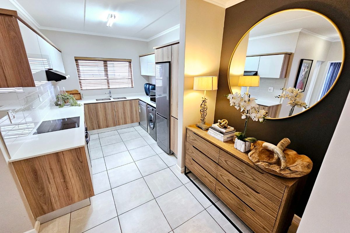 Modern kitchen featuring sleek wood-grain and white cabinetry, stone countertops, integrated hob, and tiled flooring, offering a clean and functional culinary space.