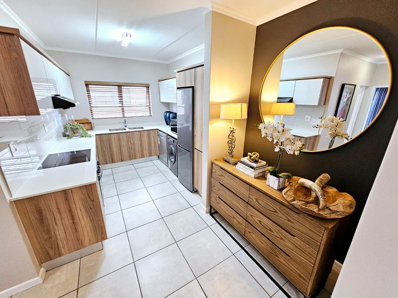 Modern kitchen featuring sleek wood-grain and white cabinetry, stone countertops, integrated hob, and tiled flooring, offering a clean and functional culinary space.