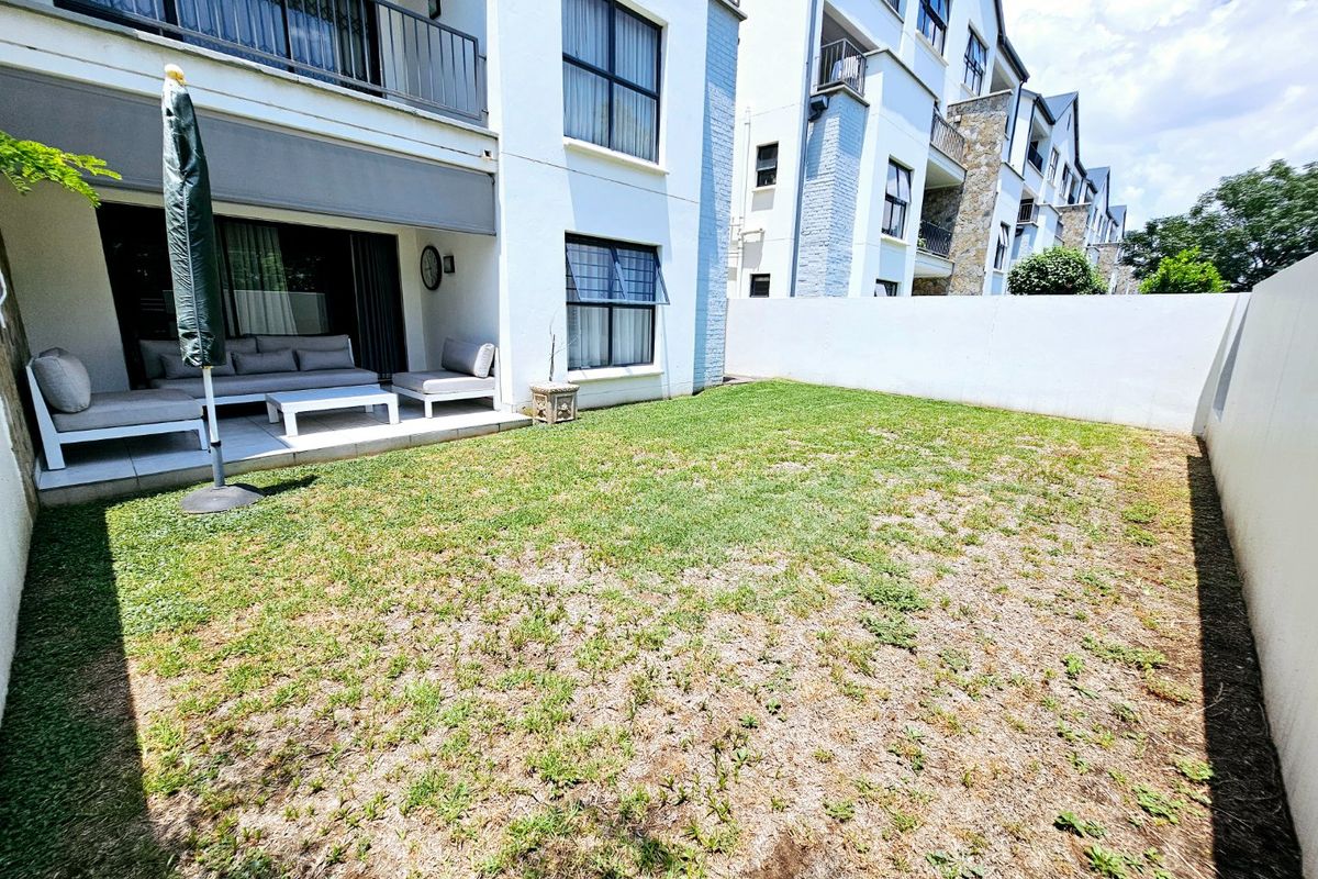 Rear view of the apartment featuring a private garden with a tiled patio area, retractable awning, and direct access via sliding glass doors.