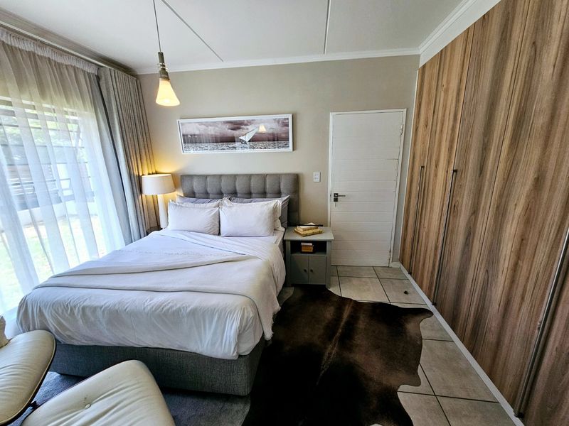 A well-maintained bedroom featuring built-in wooden cupboards, tiled flooring, and a sliding door providing access to the exterior.