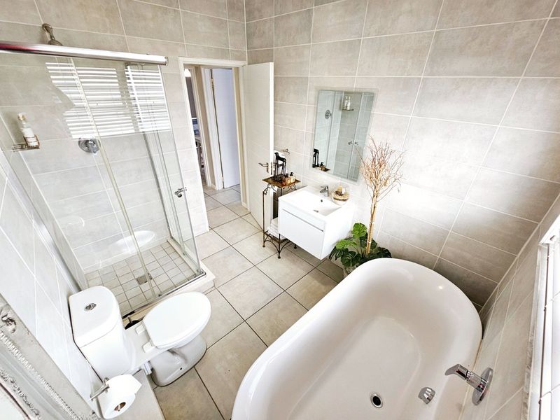 Modern bathroom featuring a freestanding bathtub, glass-enclosed shower, wall-mounted vanity, and neutral floor-to-ceiling tiling.