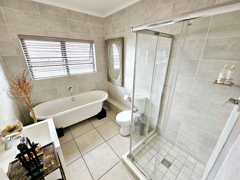 A well-maintained bathroom featuring a freestanding bathtub, a separate glass-enclosed shower, and neutral floor-to-ceiling tiling.
