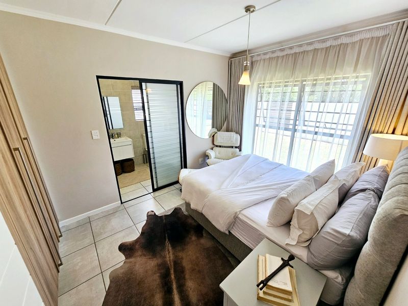 A well-maintained bedroom featuring tiled flooring, built-in cupboards, and a sliding glass door providing access to an en-suite bathroom.