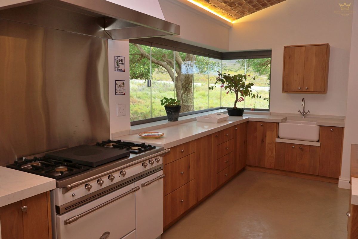 Modern farmhouse kitchen featuring wooden cabinetry, stone countertops, a gas range cooker, and a large corner window with scenic views.
