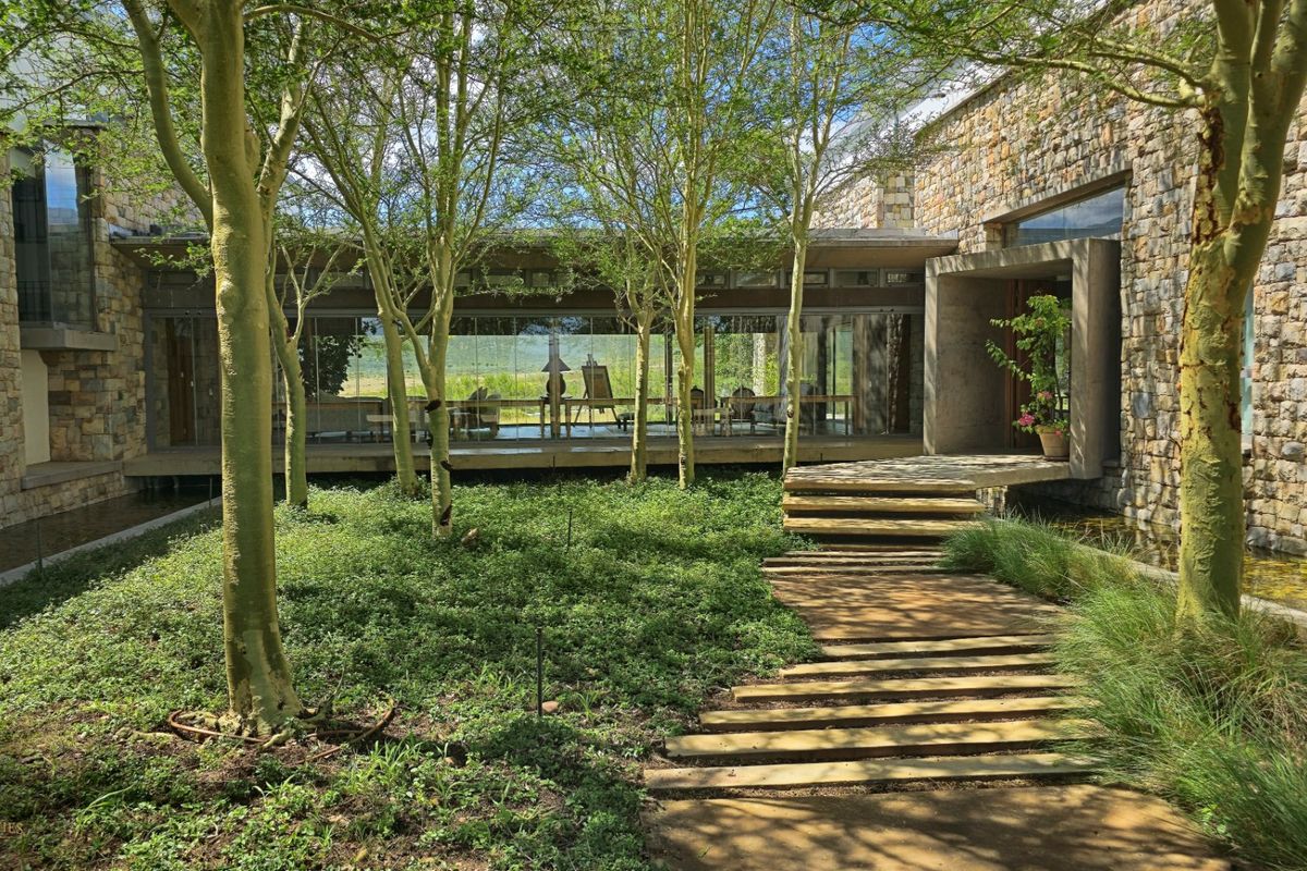 A serene courtyard featuring stone-clad walls, a concrete walkway, and floor-to-ceiling glass windows overlooking a lush, tree-filled garden.