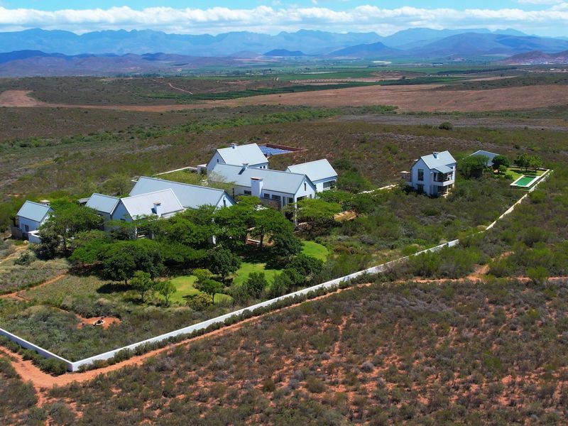 Aerial view of a sprawling farm estate featuring multiple buildings, a swimming pool, and expansive landscaped grounds set against a mountain backdrop.
