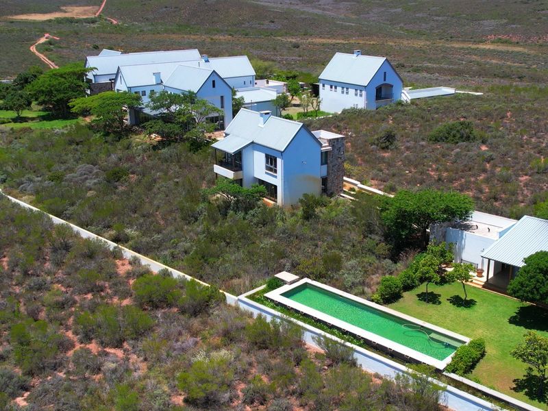 Aerial view of a farm property featuring multiple white buildings with metal roofs, a swimming pool, and solar panels set in a rural landscape.