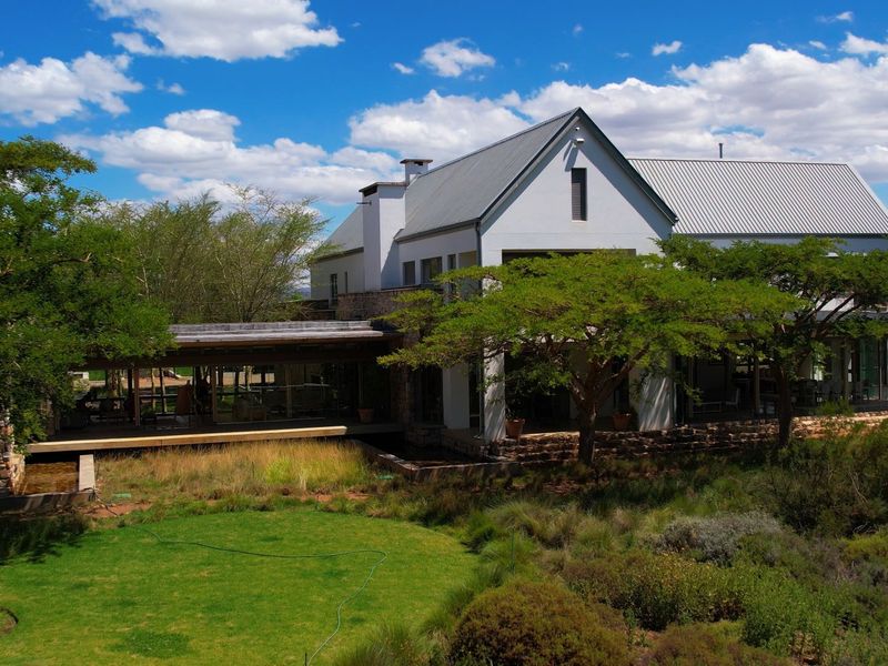 A rear view of a modern farmhouse featuring stone cladding, a metal roof, and a spacious covered patio overlooking a well-maintained garden.