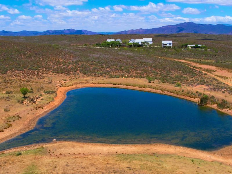 An aerial view of a large farm dam set within a vast, open landscape with the main farmhouse buildings visible in the distance.