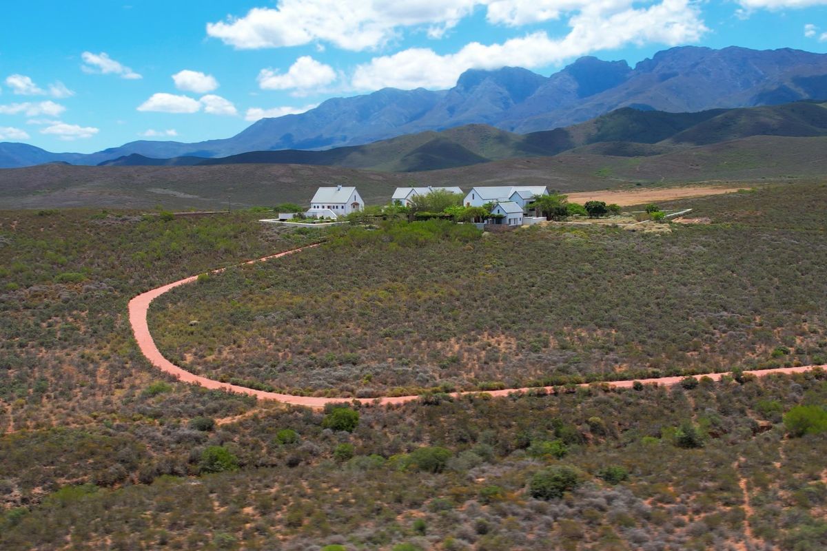 Aerial view of a farm property featuring multiple buildings with pitched roofs, set within a vast landscape with a long gravel driveway.