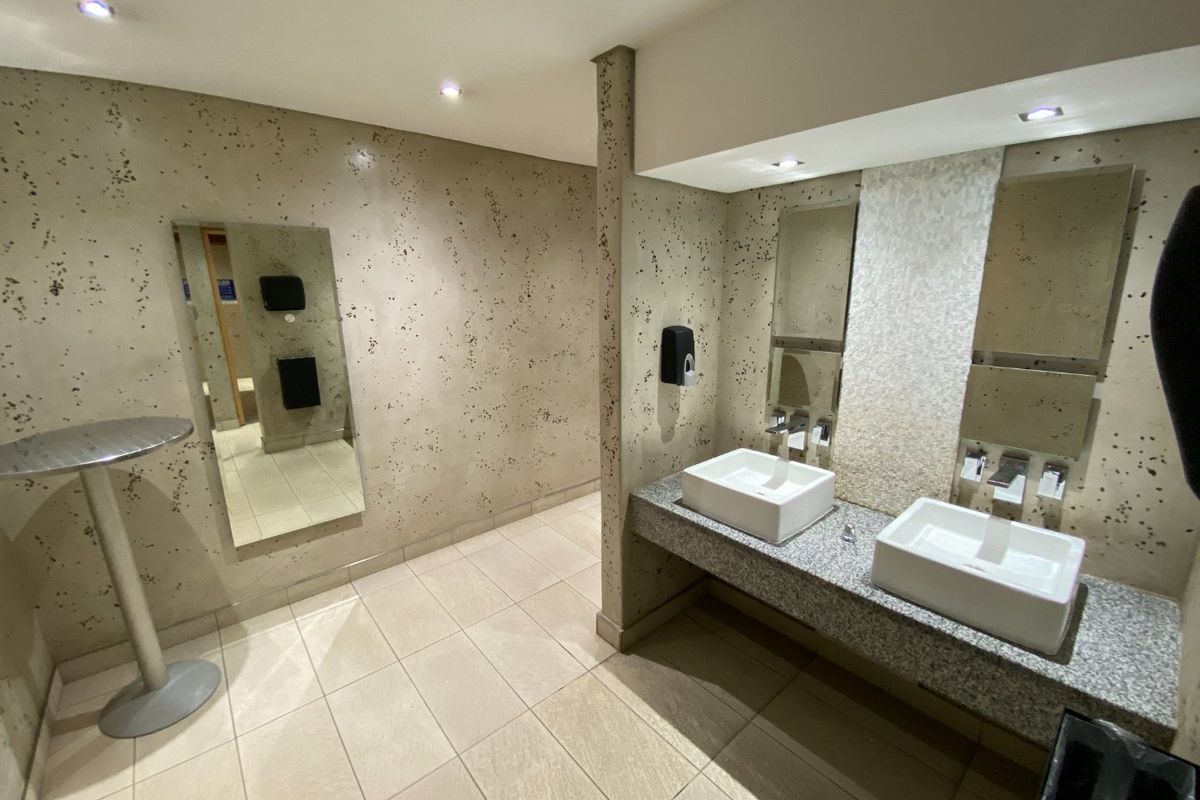 A modern commercial bathroom featuring a dual vessel sink vanity with granite countertop, recessed lighting, and contemporary textured wall finishes.