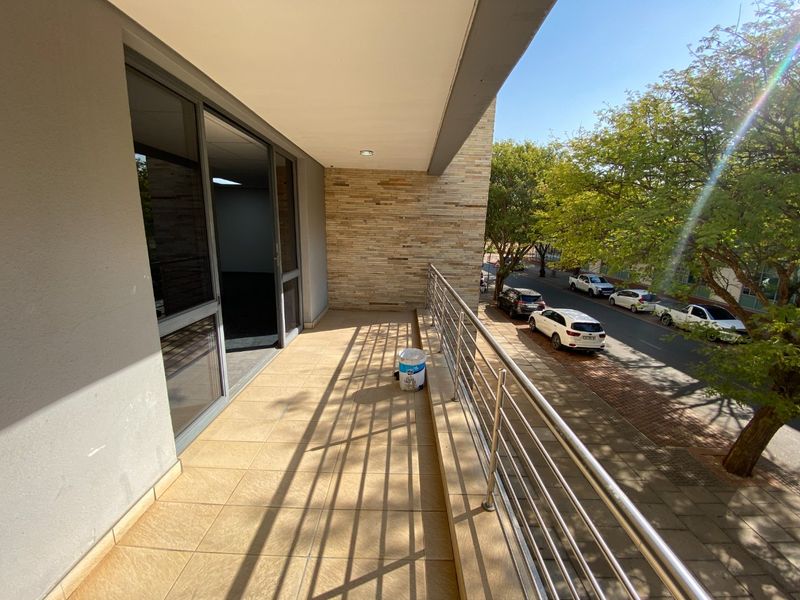 A spacious covered balcony featuring tiled flooring, a modern stainless steel balustrade, and a decorative stone-clad feature wall overlooking the street.