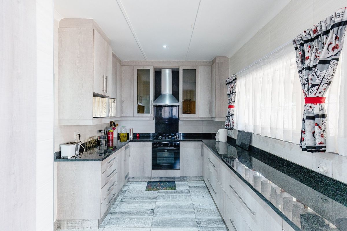 A well-maintained kitchen featuring light wood-finish cabinetry, dark granite countertops, a built-in oven, gas hob, and a stainless steel extractor fan.
