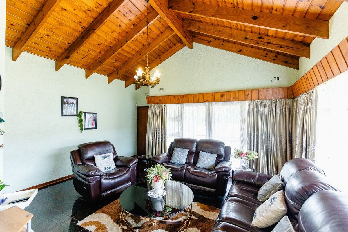 Spacious living room featuring a high vaulted timber ceiling with exposed beams, tiled flooring, and classic timber wall accents.