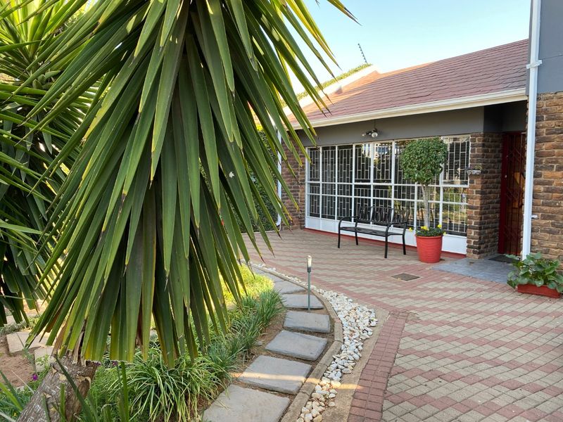 A paved outdoor patio area featuring a brick facade, security-barred windows, and a landscaped garden path leading to the entrance.