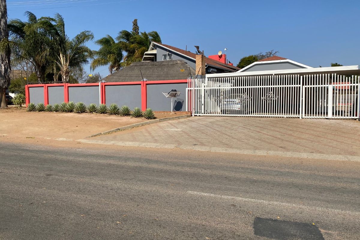 Front view of the property featuring a paved driveway, secure metal gate, and a perimeter wall with electric fencing.