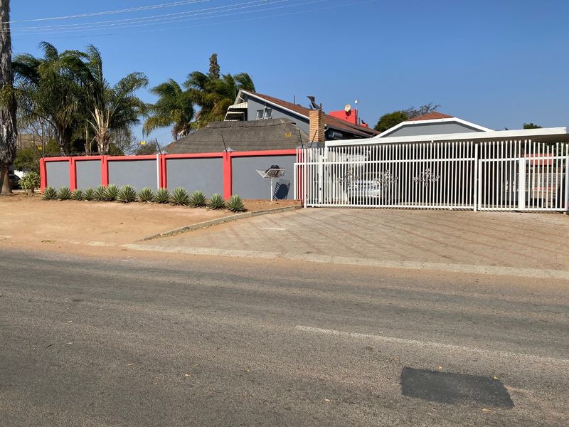 Front view of the property featuring a paved driveway, secure metal gate, and a perimeter wall with electric fencing.