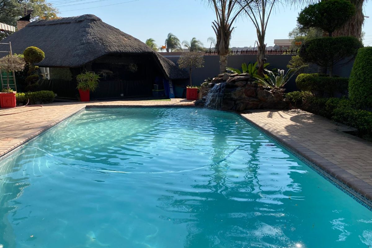 Outdoor pool area featuring a swimming pool with a rock water feature and an adjacent thatched lapa, set within a landscaped garden.
