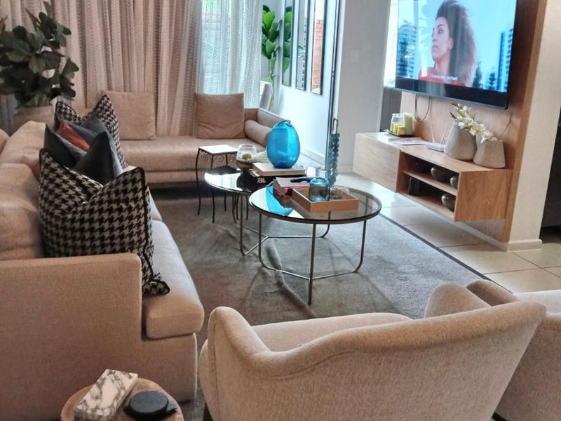 A well-maintained living room featuring a modern built-in media wall, tiled flooring, and large sliding glass doors leading to an outdoor area.
