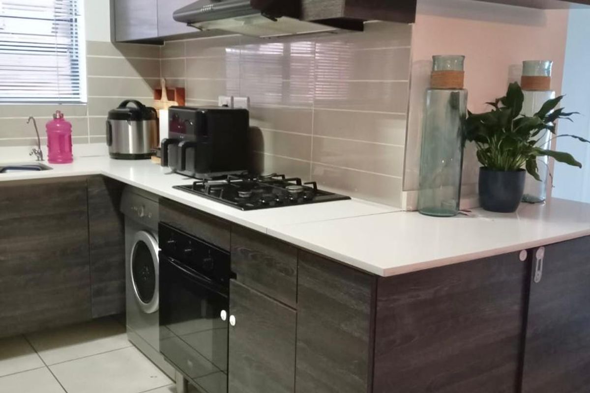 Modern kitchen featuring dark wood-grain cabinetry, white countertops, gas hob, built-in oven, extractor fan, and integrated laundry appliance.
