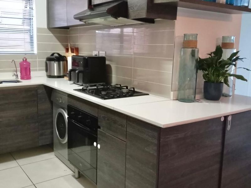Modern kitchen featuring dark wood-grain cabinetry, white countertops, gas hob, built-in oven, extractor fan, and integrated laundry appliance.