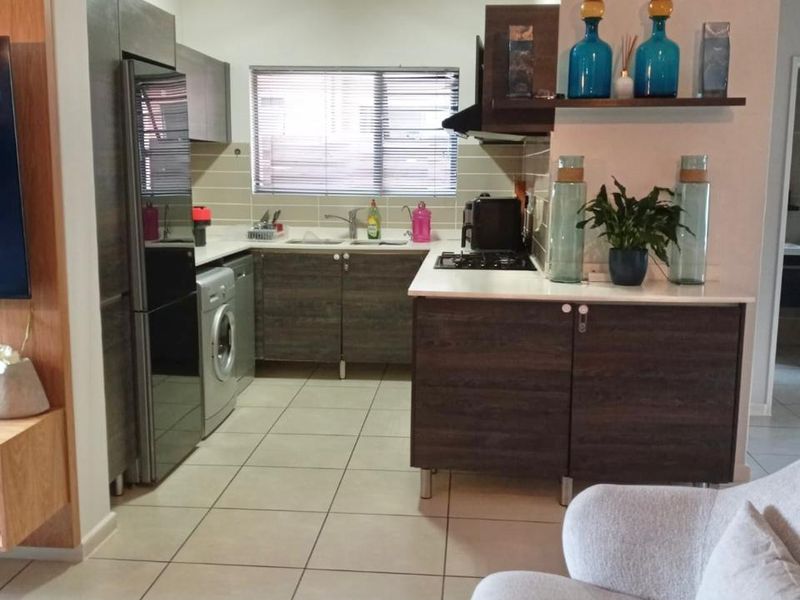 Compact kitchen featuring dark wood-look cabinetry, tiled flooring, integrated gas hob, extractor fan, and a stainless steel sink with a window view.