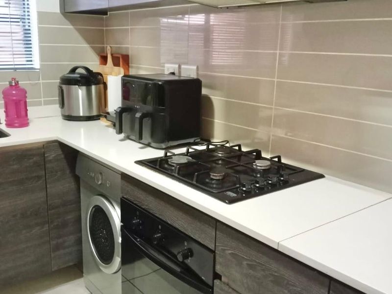 Modern kitchen featuring dark wood-grain cabinetry, stone countertops, a gas hob, built-in oven, extractor fan, and an integrated washing machine.