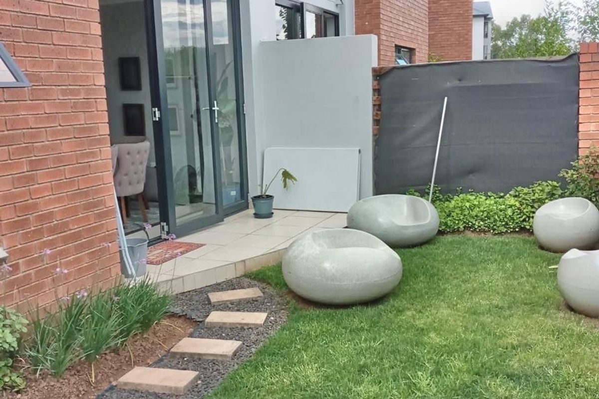 A private rear garden featuring a paved patio area, stone walkway, and lawn, accessible via glass sliding doors from the apartment.