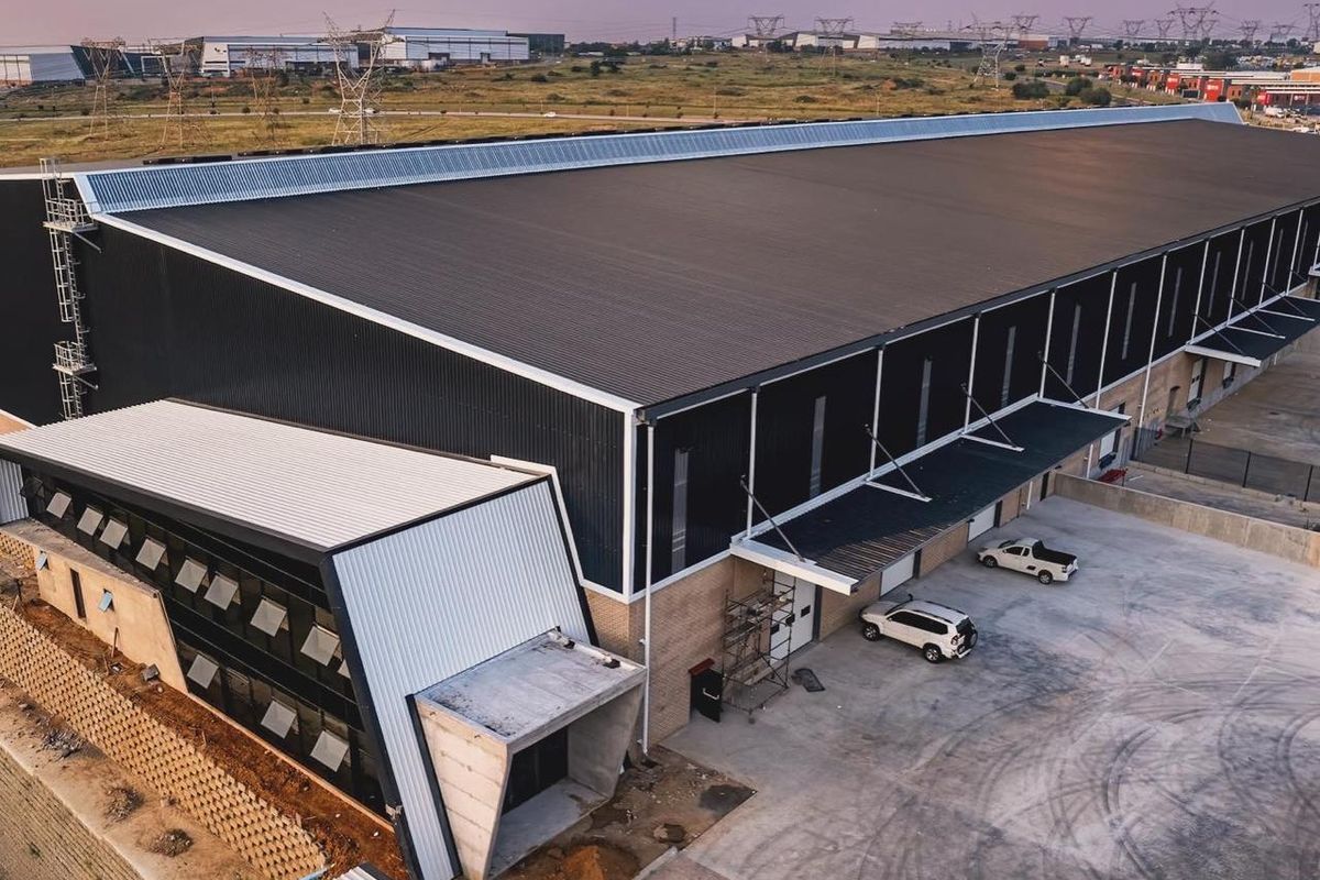 Aerial view of a modern industrial warehouse facility featuring a large corrugated metal roof, concrete loading area, and integrated office section.