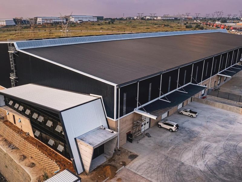 Aerial view of a modern industrial warehouse facility featuring a large corrugated metal roof, concrete loading area, and integrated office section.