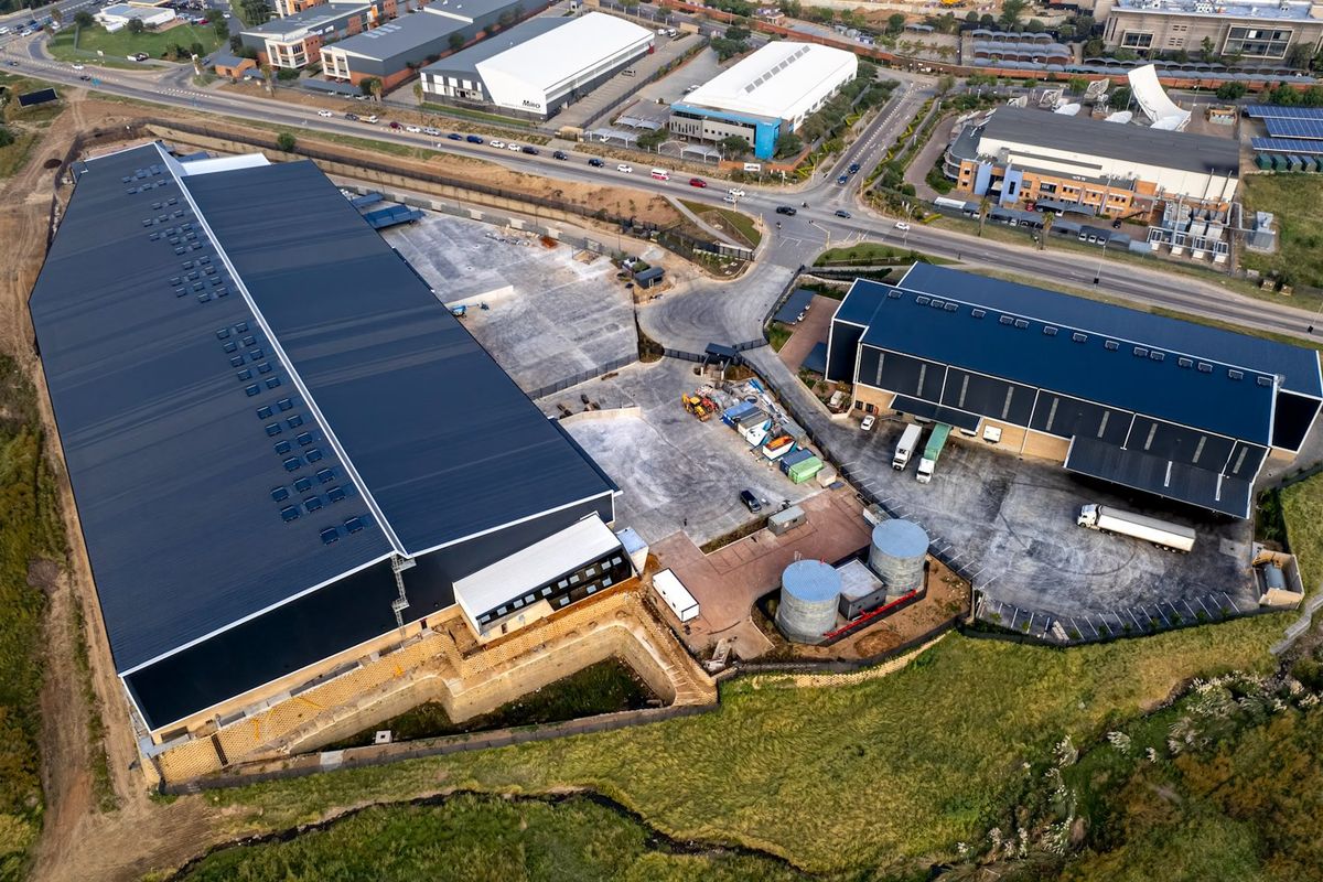 Aerial view of an industrial property featuring two large warehouse buildings, paved yard space, loading bays, and water storage tanks.