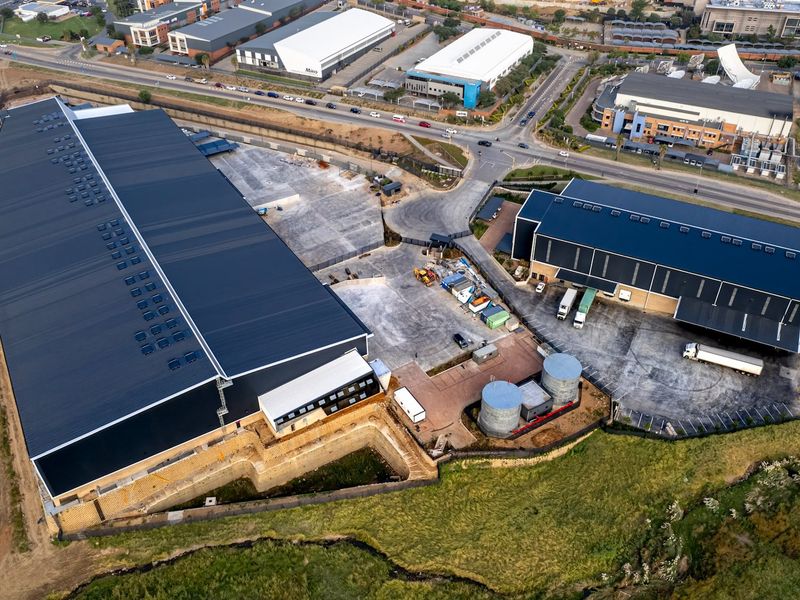 Aerial view of an industrial property featuring two large warehouse buildings, paved yard space, loading bays, and water storage tanks.