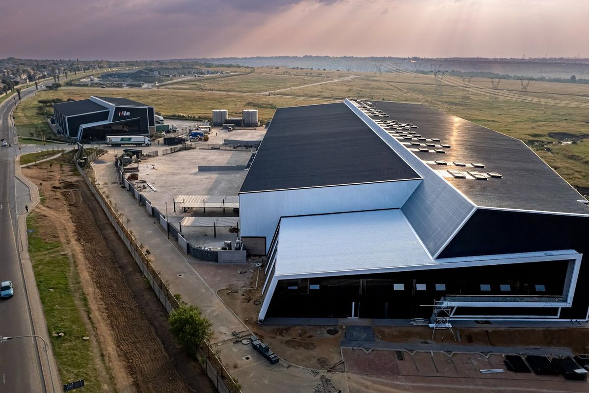 Aerial view of a modern industrial facility featuring large warehouse structures, paved yard space, and perimeter security fencing in a commercial estate setting.