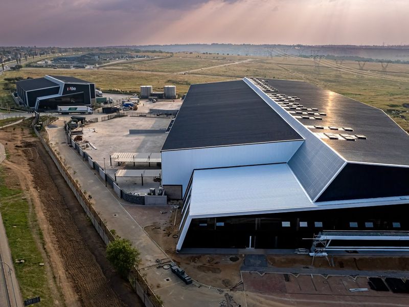 Aerial view of a modern industrial facility featuring large warehouse structures, paved yard space, and perimeter security fencing in a commercial estate setting.