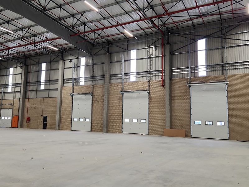 Spacious industrial warehouse interior featuring high ceilings, exposed steel trusses, concrete flooring, and multiple roller shutter doors for efficient logistics access.