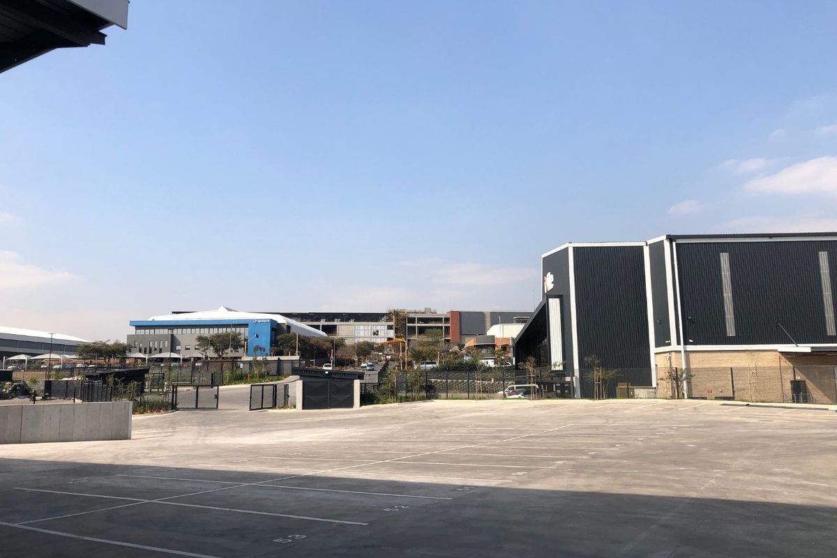 A view of the industrial property's rear yard featuring a large concrete paved area, marked parking bays, and modern metal-clad industrial buildings.