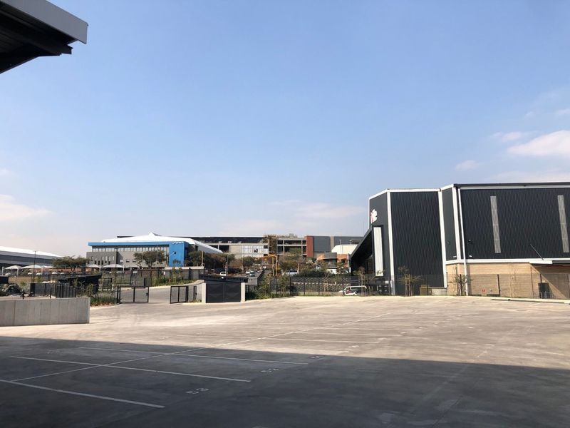 A view of the industrial property's rear yard featuring a large concrete paved area, marked parking bays, and modern metal-clad industrial buildings.