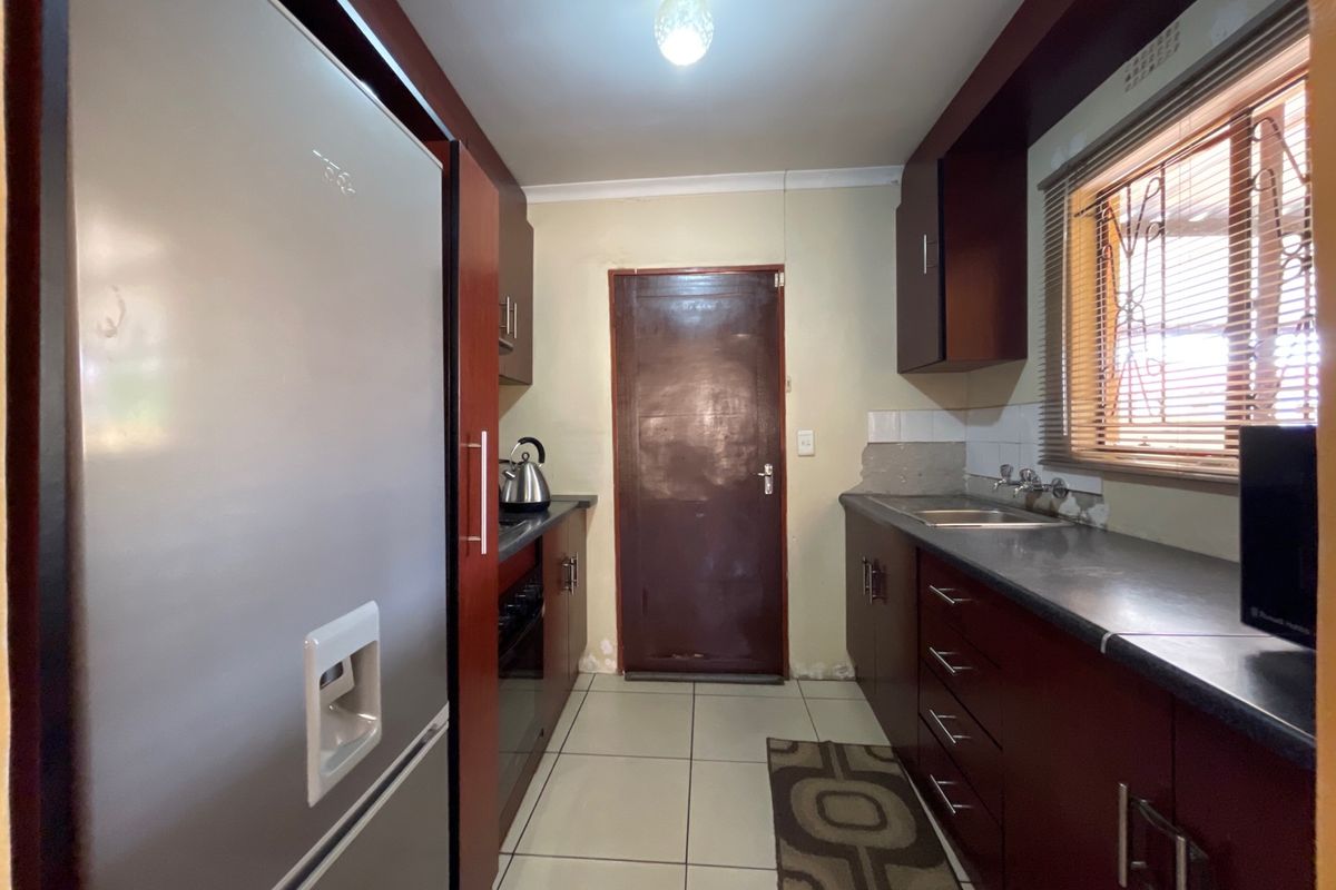 A functional galley-style kitchen featuring dark wood cabinetry, laminate countertops, tiled flooring, and a rear access door.