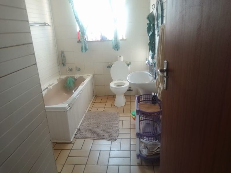 A functional bathroom featuring a bathtub, pedestal basin, and toilet with tiled flooring and wall finishes, showing signs of wear on the bathtub.