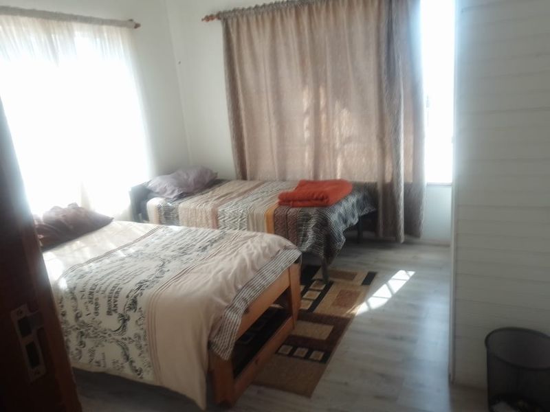 A bedroom featuring laminate flooring and dual windows with curtain rods, currently configured with two single beds.