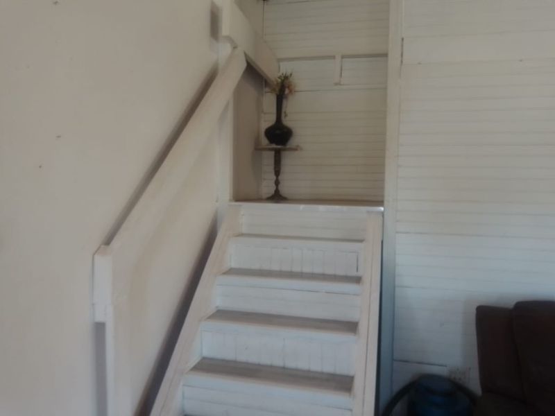 A simple interior staircase featuring white painted wooden paneling and a matching handrail, showing signs of wear and requiring cosmetic updates.