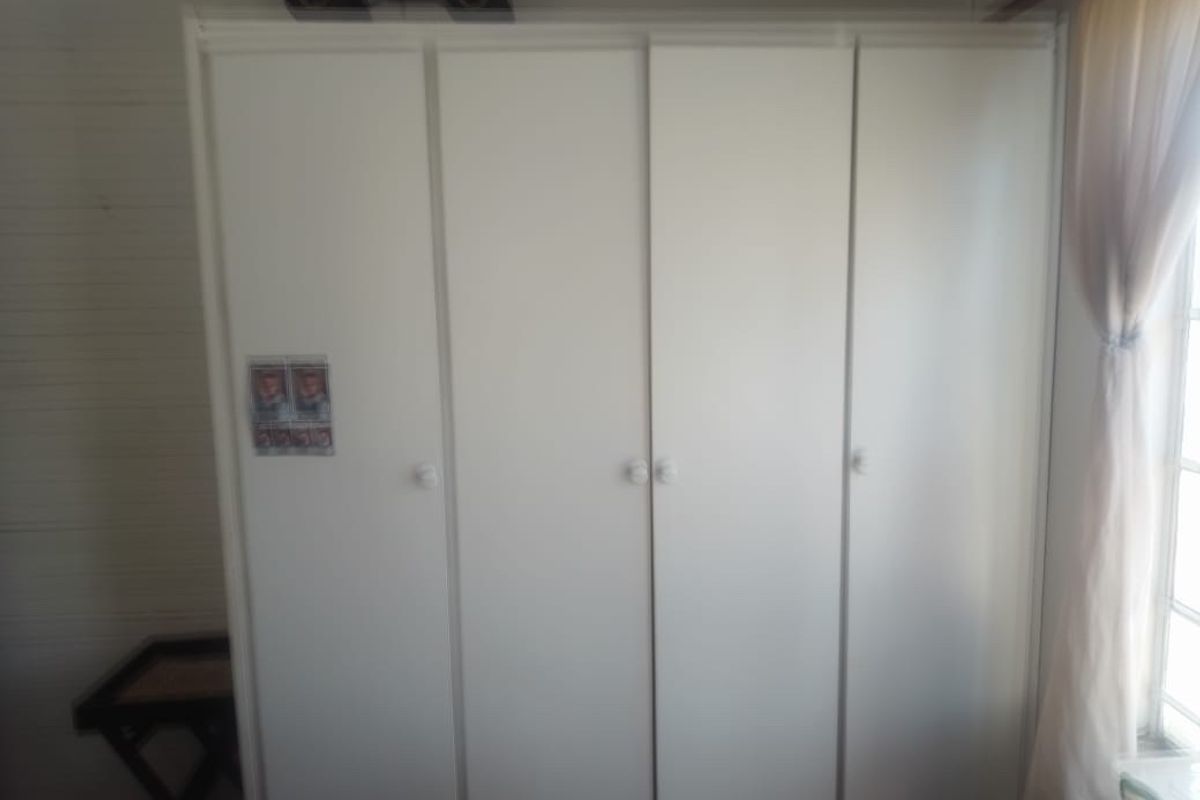 A bedroom featuring a white built-in wardrobe with multiple doors.