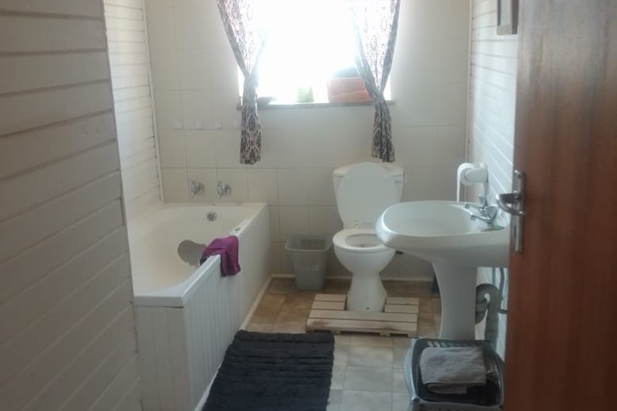 A functional bathroom featuring a bathtub, pedestal basin, and toilet, finished with tiled walls and timber paneling. The space would benefit from modern updates.