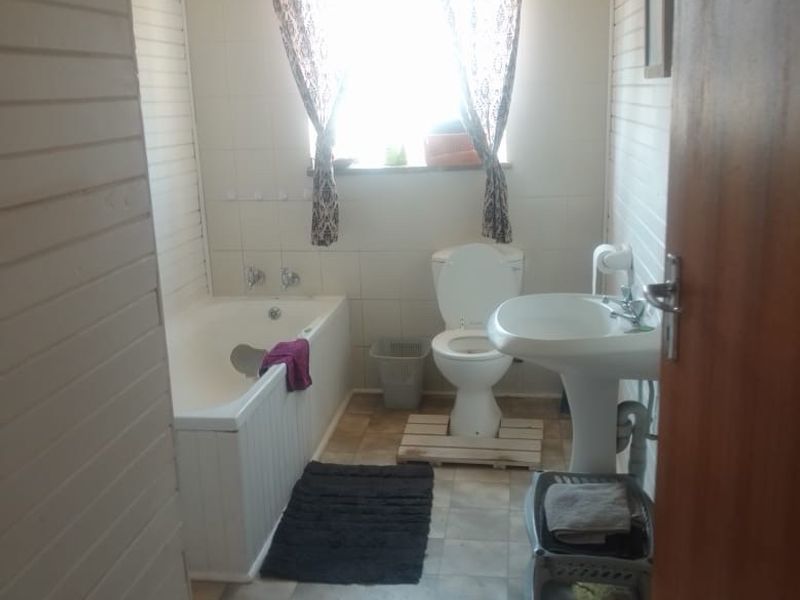 A functional bathroom featuring a bathtub, pedestal basin, and toilet, finished with tiled walls and timber paneling. The space would benefit from modern updates.