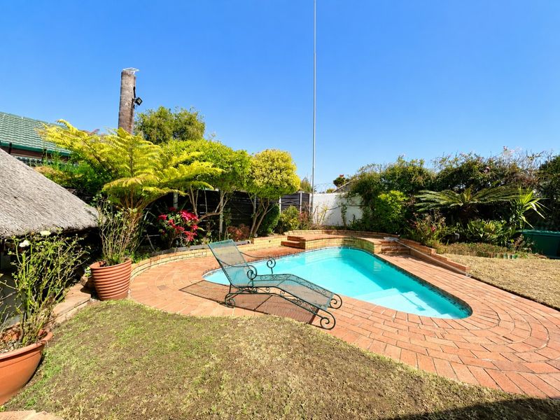 Outdoor pool area featuring a swimming pool with brick paving surround and a low brick retaining wall in a landscaped garden setting.