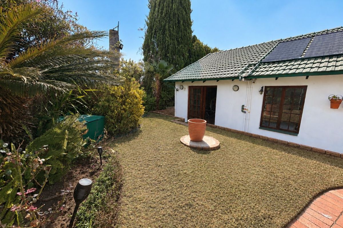 Rear view of the property featuring a tiled roof with solar panels, timber-framed windows and doors, and a landscaped garden with brick paving.